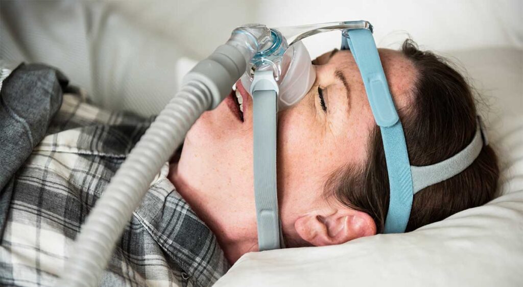 A person wears an anti-snoring chin strap—a common tool in managing sleep apnea. But what exactly is sleep apnea? It’s more than snoring; it’s a serious condition that affects breathing during sleep and can impact overall health.