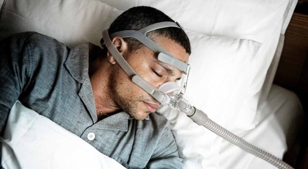 A man wearing an oxygen mask represents common treatments for sleep apnea and sinusitis. CPAP therapy helps keep airways open for sleep apnea patients, while sinusitis sufferers may need interventions to ease breathing.